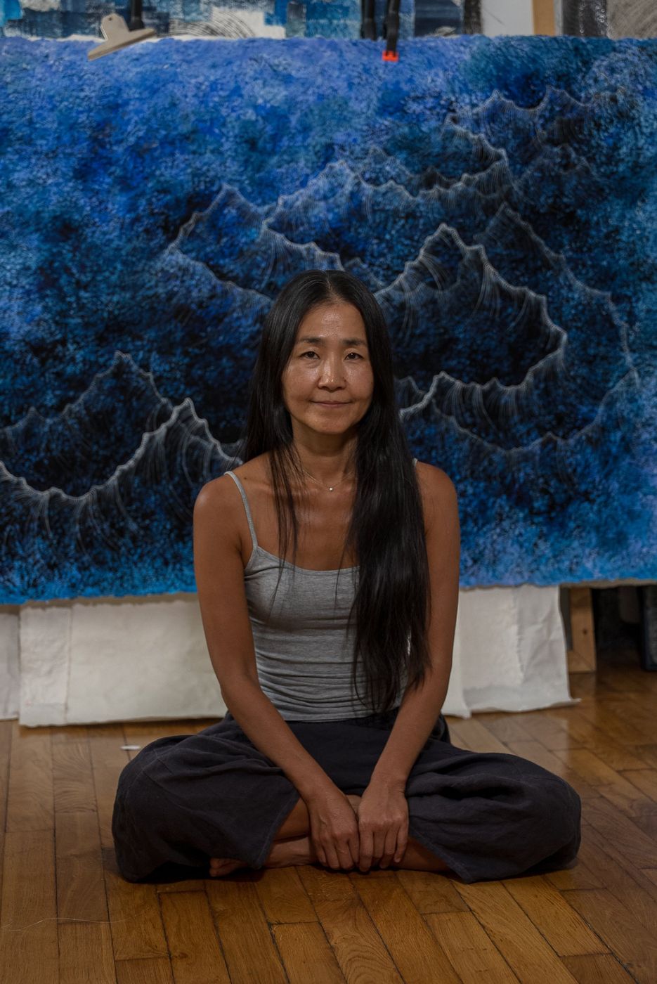 Portrait d’une artiste assise devant une grande œuvre textile bleue