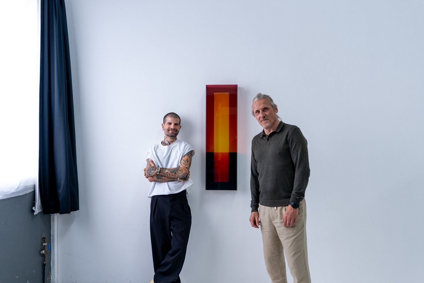 Portrait de deux personnes devant une œuvre murale dans un atelier